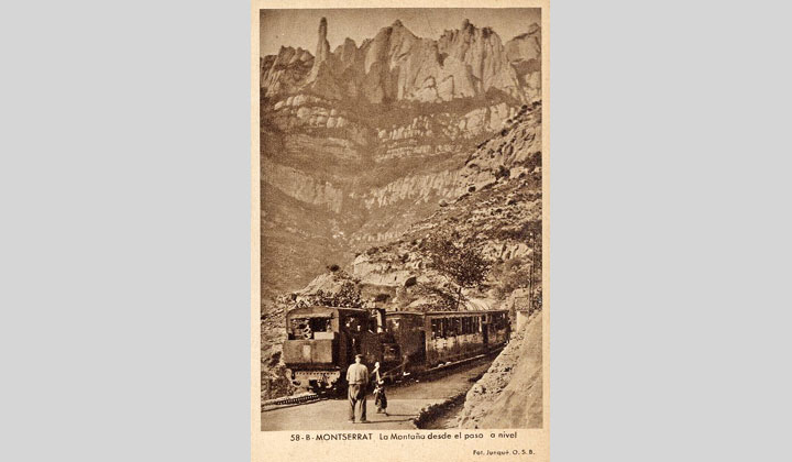 Vista desde el paso a nivel del ferrocarril de cremallera de v�a estrecha y la monta�a de Montserrat. Locomotora de vapor Tipo 0-2-1 invertida remolcando dos coches de viajeros. En el centro, el perro guardabarrera. Archivo Hist�rico Ferroviario TP-MR-0706